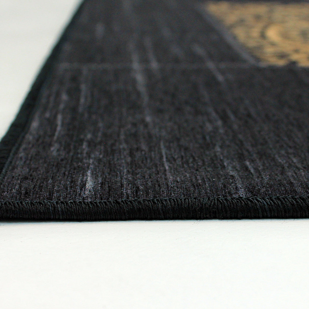 Esquina de la alfombra 'Mosaic', mostrando los detalles del diseño intrincado con patrones dorados. Esta elegante alfombra añade distinción a cualquier espacio y es lavable en lavadora para facilitar su cuidado.