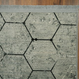 Esquina de la alfombra 'Terra', mostrando el patrón geométrico hexagonal en tonos grises que añade sofisticación y un toque moderno a la decoración.